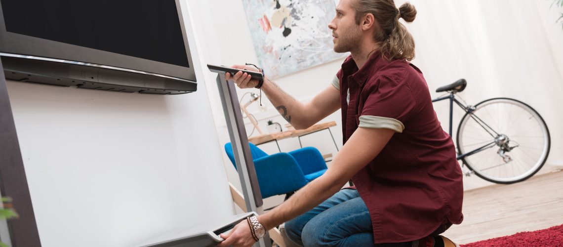 handsome man with remote control and television at home
