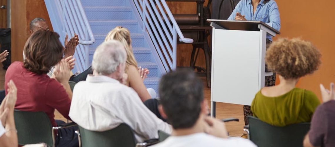 Woman At Podium Chairing Neighborhood Meeting In Community Centre