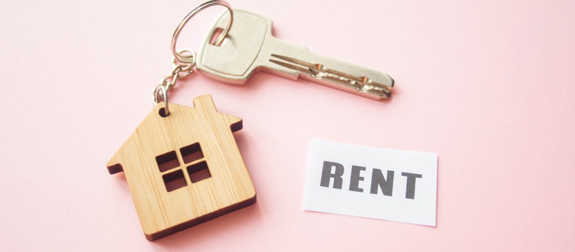 Wooden house toy and silver key on bright pink background with phrase quote Rent. Mortgage, house buy sell, investment, rent, realtor concept