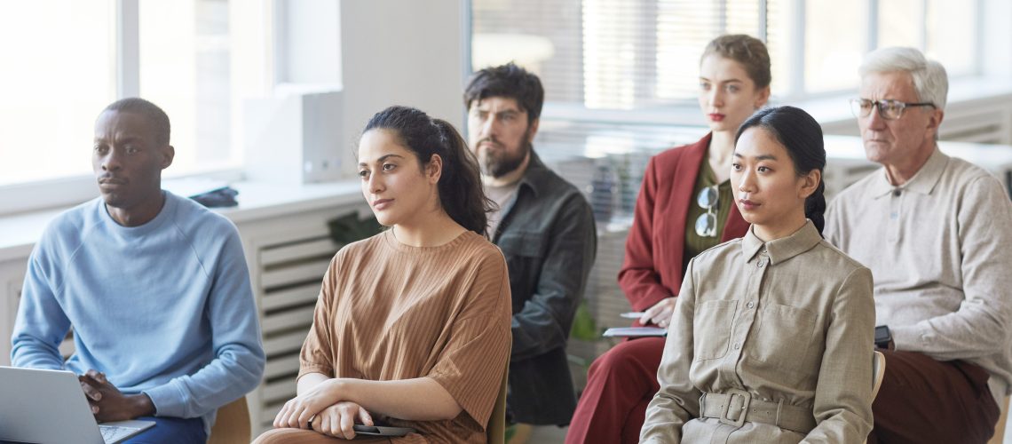 Diverse group of business people sitting on chairs in audience and listening at meeting or seminar