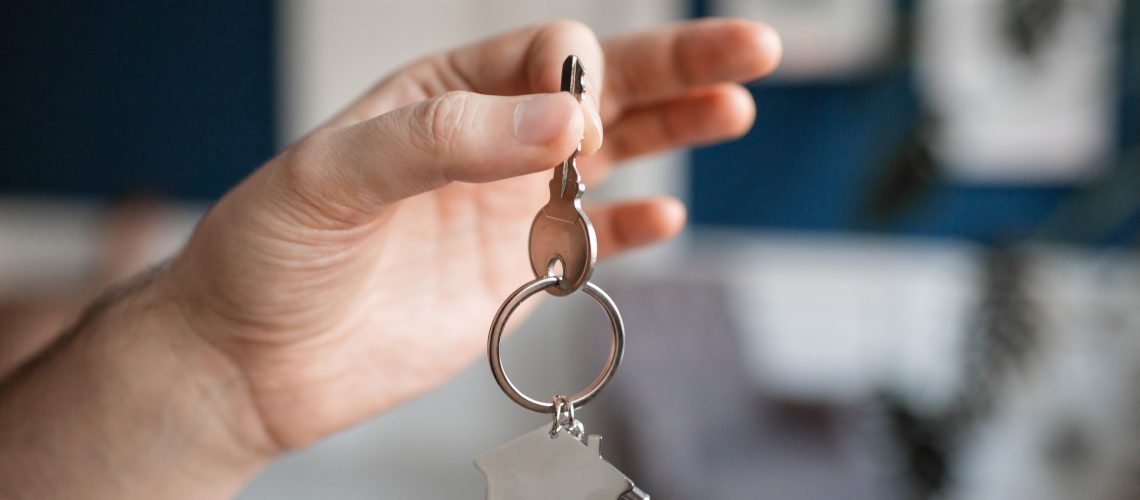 House key and keychain in the form of homes lies on wooden boards. Concept for real estate, moving home or renting property. Copy space